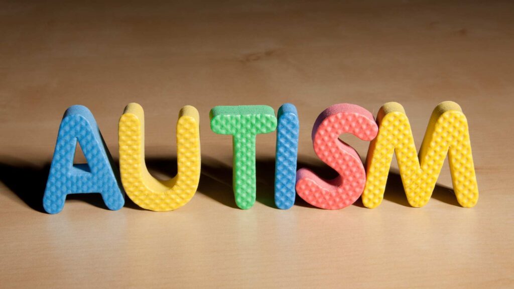 Letras de colores que forman la palabra “AUTISM” sobre una mesa de madera.
