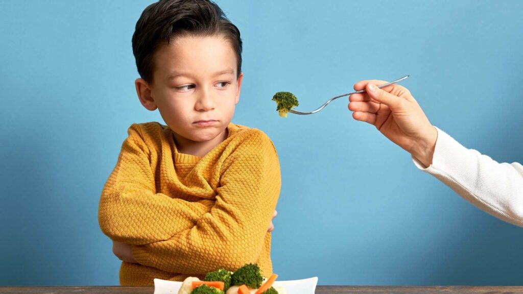 Niño con expresión de rechazo frente a verduras, ilustrando la alimentación selectiva en niños con autismo